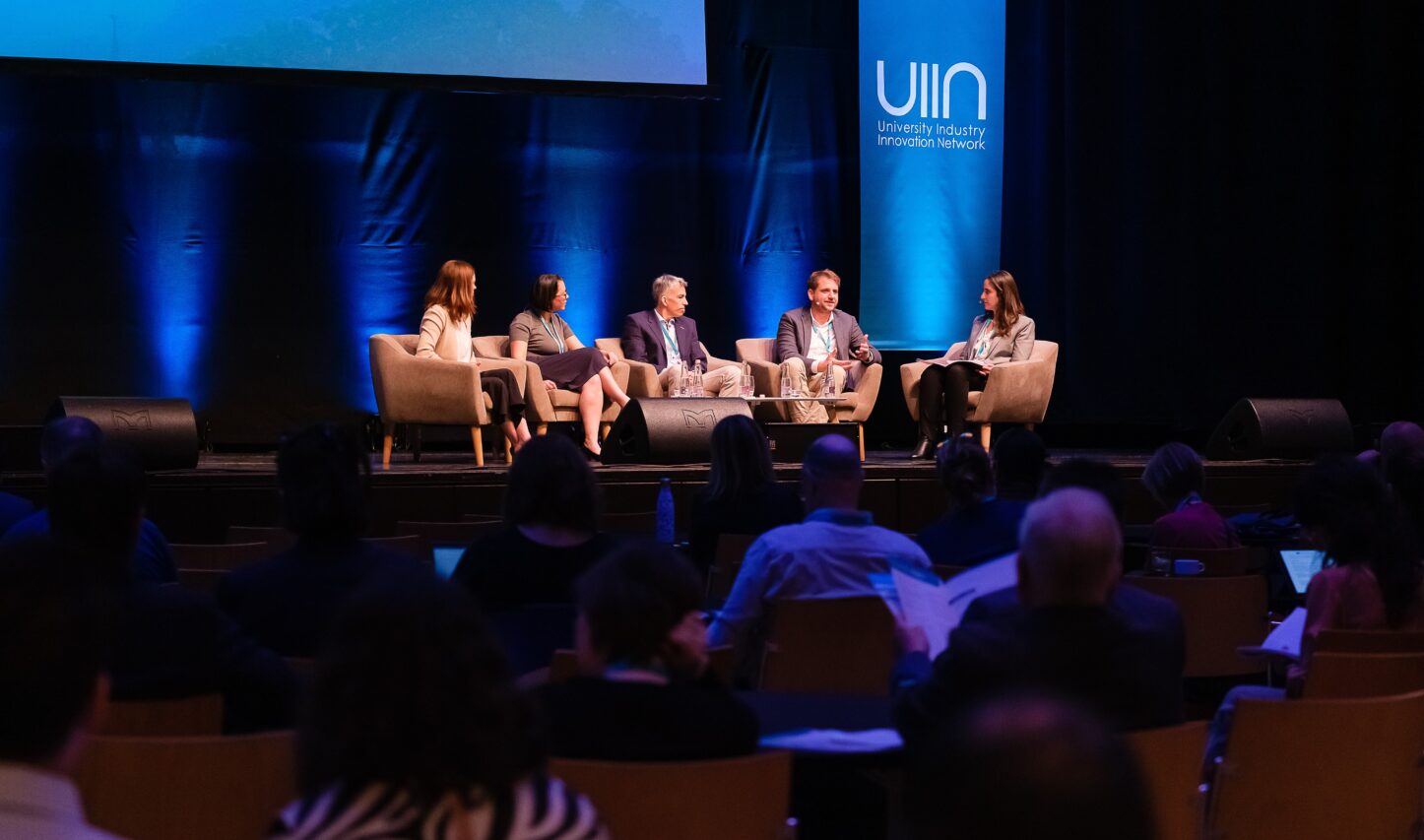 Five panel guest speakers from UIIN sitting on stage with UIIN branding in background