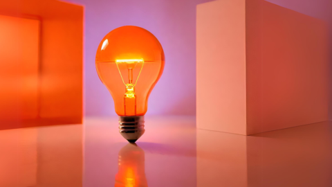Orange lightbulb sits in front of orange boxes and a purple background